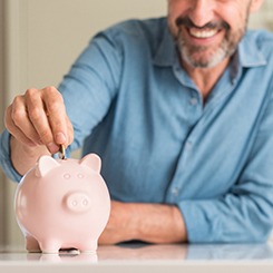 Nose down view of a man in a blue shirt putting a coin into a pink piggy bank