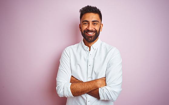 Man in white shirt crossing arms and smiling in front of pink background