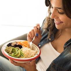 Woman in denim eating healthy foods from a red-rimmed bowl