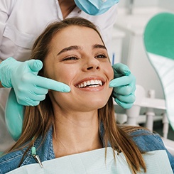 Woman in denim jacket in dental chair smiling as dentist points to her teeth