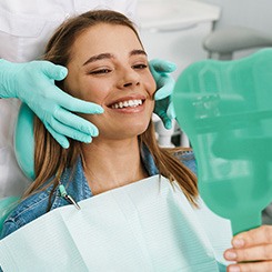 Woman smiling at reflection in handheld mirror